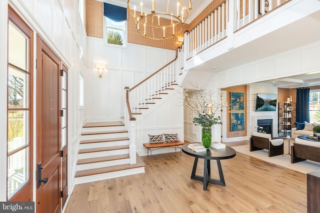 foyer entrance featuring a towering ceiling, stairs, light wood-style floors, a fireplace, and a decorative wall