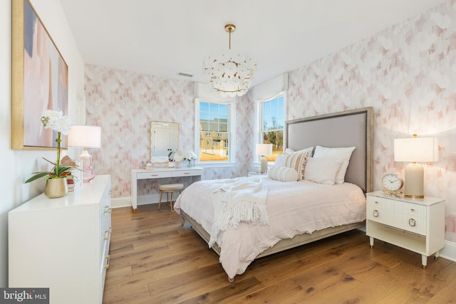 bedroom featuring wallpapered walls, baseboards, visible vents, wood finished floors, and a chandelier