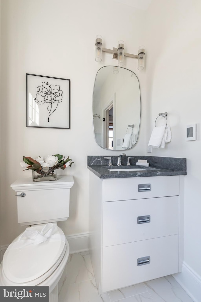 bathroom with toilet, marble finish floor, baseboards, and vanity