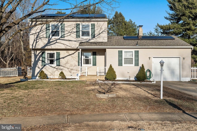 traditional-style home featuring a garage, solar panels, concrete driveway, fence, and a front lawn