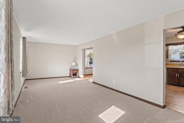 empty room featuring light carpet, baseboards, and a sink