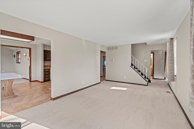 empty room with visible vents, light carpet, stairway, and baseboards