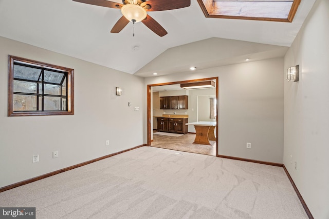 empty room featuring a ceiling fan, light colored carpet, vaulted ceiling, and baseboards