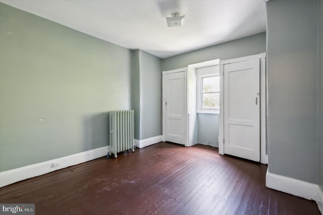 unfurnished bedroom featuring radiator, baseboards, and dark wood finished floors