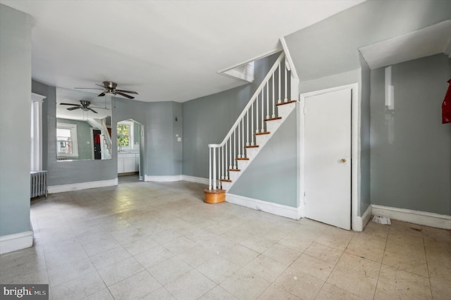 unfurnished living room featuring radiator, stairway, ceiling fan, baseboards, and tile patterned floors