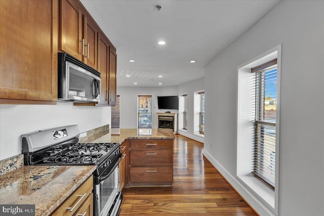 kitchen with stainless steel appliances, open floor plan, dark wood finished floors, and light stone countertops