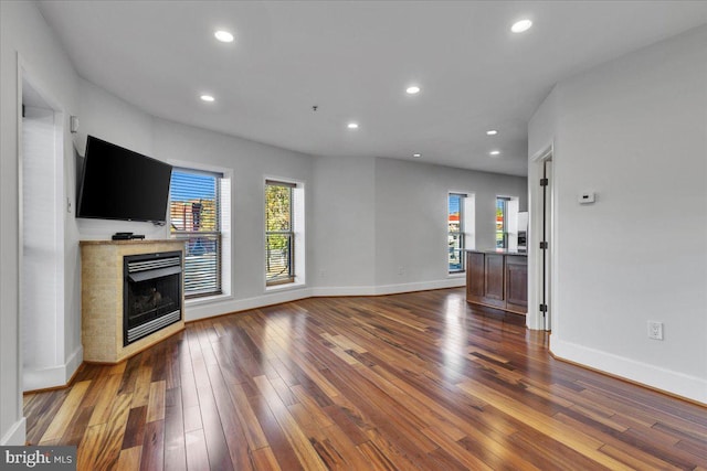 unfurnished living room with a healthy amount of sunlight, a tile fireplace, dark wood finished floors, and recessed lighting