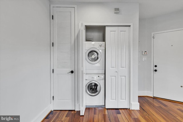 clothes washing area with stacked washer / dryer, laundry area, baseboards, and wood finished floors