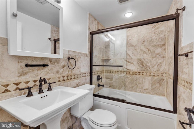 full bathroom featuring a sink, shower / bath combination with glass door, toilet, and tile walls