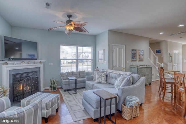 living room featuring wood finished floors, visible vents, a lit fireplace, and stairs