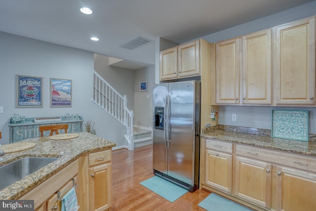 kitchen featuring light brown cabinetry, light stone counters, stainless steel refrigerator with ice dispenser, and visible vents