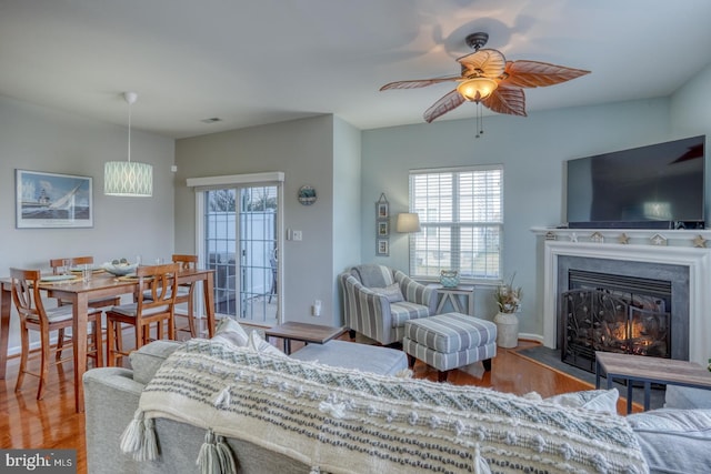 living room with a fireplace with flush hearth, a ceiling fan, visible vents, and wood finished floors