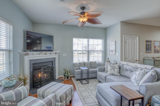 living area featuring a fireplace with flush hearth, a ceiling fan, and wood finished floors