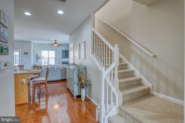 stairs featuring baseboards, a ceiling fan, hardwood / wood-style flooring, a fireplace, and recessed lighting