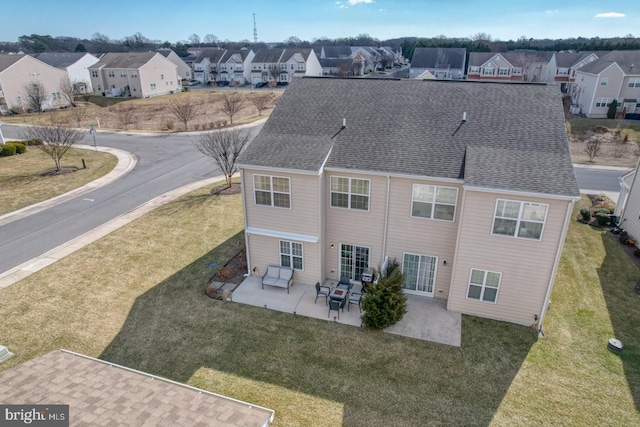 rear view of property featuring a yard, roof with shingles, a patio area, and a residential view