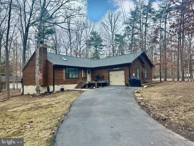 chalet / cabin with a chimney, an attached garage, and aphalt driveway