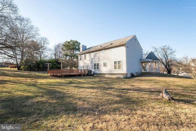 back of property with a deck, a chimney, and a yard