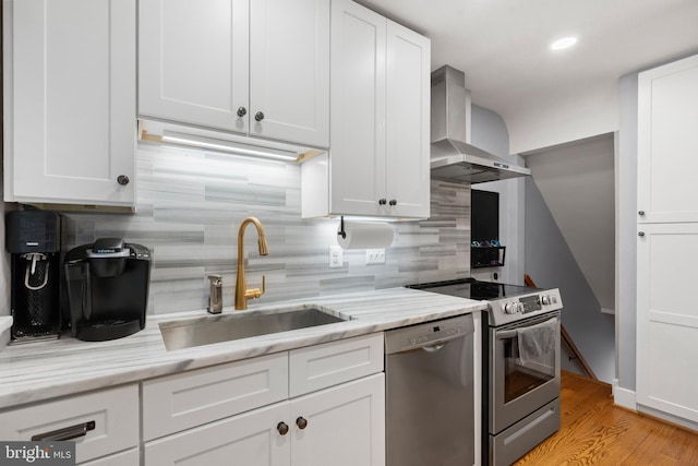 kitchen with stainless steel appliances, white cabinets, a sink, and wall chimney exhaust hood