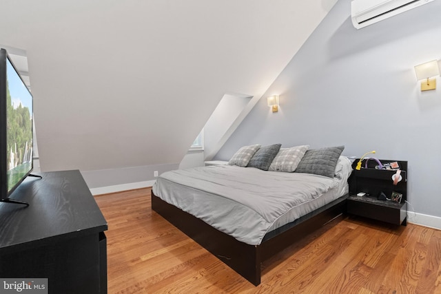 bedroom featuring light wood-style floors, an AC wall unit, multiple windows, and baseboards