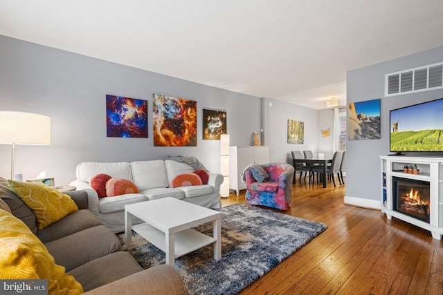 living room featuring a glass covered fireplace, baseboards, visible vents, and hardwood / wood-style floors