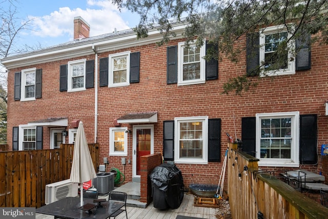 view of front of house featuring cooling unit, brick siding, fence, and a chimney