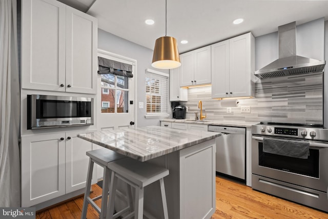 kitchen with a kitchen bar, decorative backsplash, appliances with stainless steel finishes, a sink, and wall chimney exhaust hood