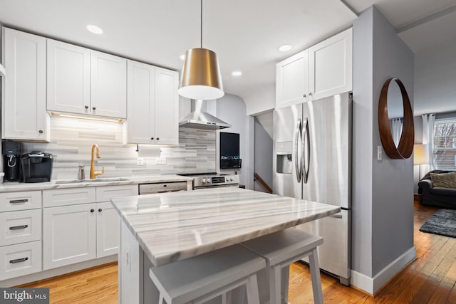 kitchen with stainless steel appliances, decorative backsplash, white cabinetry, a sink, and wall chimney exhaust hood