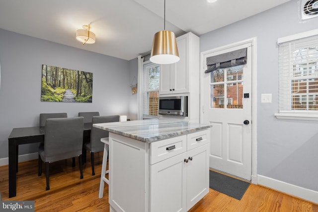 kitchen featuring light wood-type flooring, baseboards, stainless steel microwave, and white cabinets