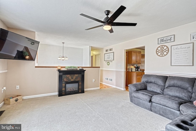 living area with a stone fireplace, light carpet, ceiling fan with notable chandelier, visible vents, and baseboards