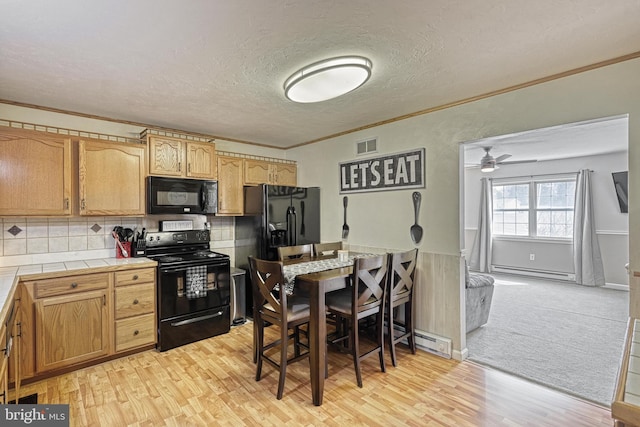 kitchen with a baseboard heating unit, ornamental molding, light wood-type flooring, tile counters, and black appliances