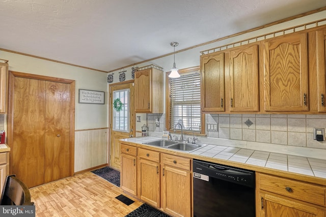 kitchen featuring tile counters, dishwasher, wainscoting, light wood-style flooring, and a sink