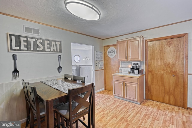 dining room featuring visible vents, a wainscoted wall, ornamental molding, a textured ceiling, and light wood-style floors