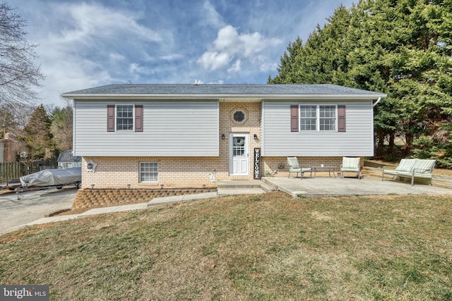 raised ranch with a patio, a front lawn, and brick siding