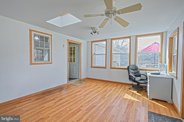 unfurnished office featuring ceiling fan, light wood-type flooring, a skylight, and baseboards