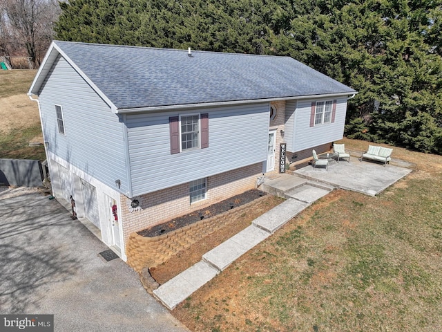 view of front of house featuring an attached garage, a shingled roof, driveway, a front lawn, and a patio area