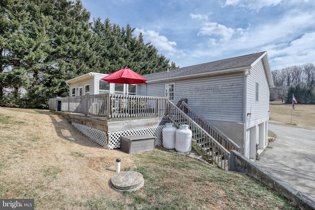 rear view of property featuring driveway, a yard, a wooden deck, and an attached garage