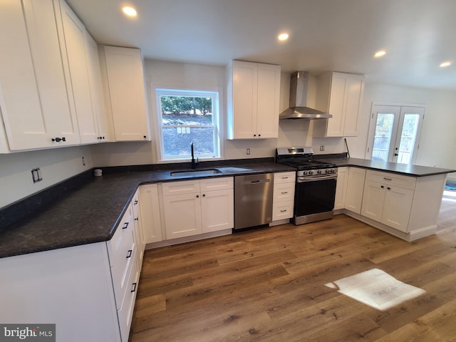 kitchen featuring a sink, dark countertops, stainless steel appliances, a peninsula, and wall chimney exhaust hood