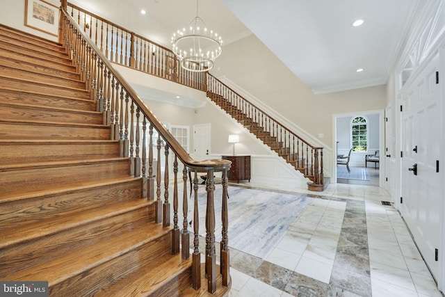 foyer entrance with crown molding, recessed lighting, stairway, a towering ceiling, and a chandelier