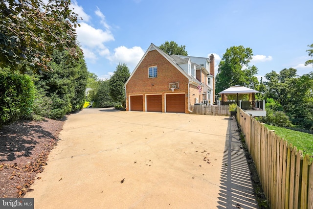 view of home's exterior featuring an attached garage, fence, concrete driveway, and brick siding