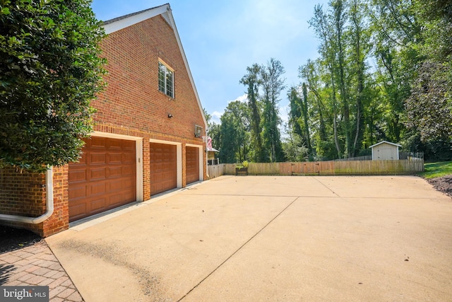 view of side of home featuring driveway, brick siding, an attached garage, and fence