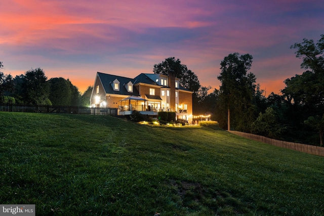 back of house at dusk featuring a yard and fence