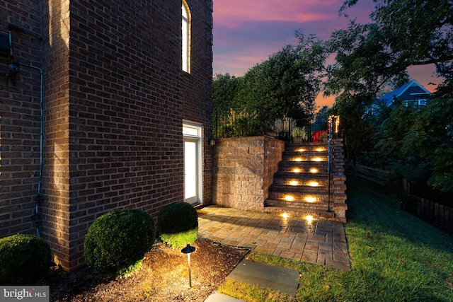 property exterior at dusk with a patio area, an outdoor fireplace, and brick siding