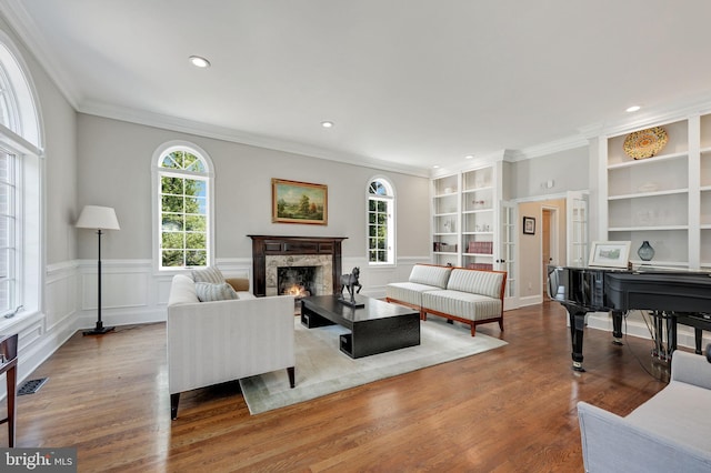 living room featuring built in features, wainscoting, wood finished floors, crown molding, and a fireplace