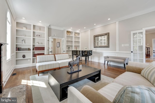 living room featuring built in features, ornamental molding, a decorative wall, and wood finished floors