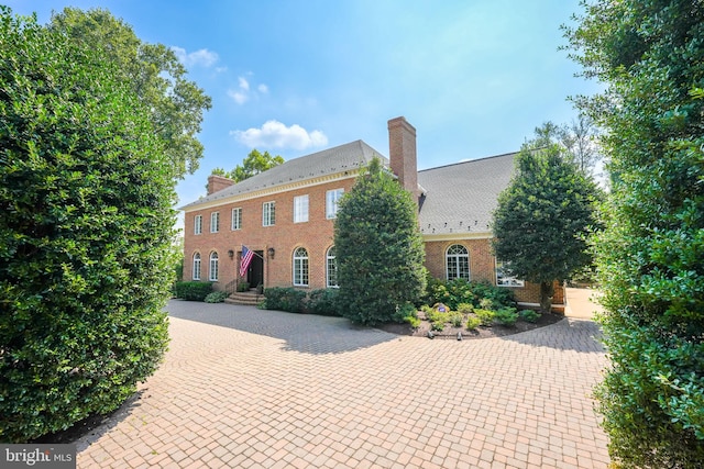 colonial inspired home with a chimney, decorative driveway, and brick siding