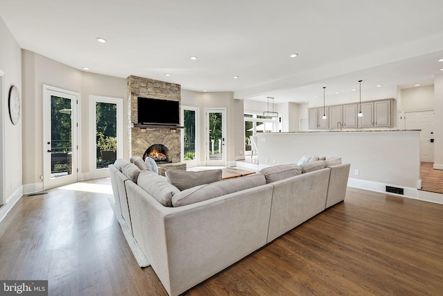 living area with recessed lighting, visible vents, a stone fireplace, and wood finished floors