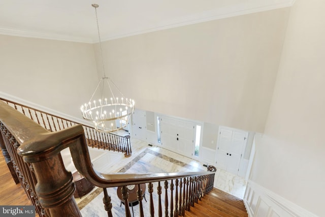 stairway featuring ornamental molding, a chandelier, a high ceiling, and wood finished floors