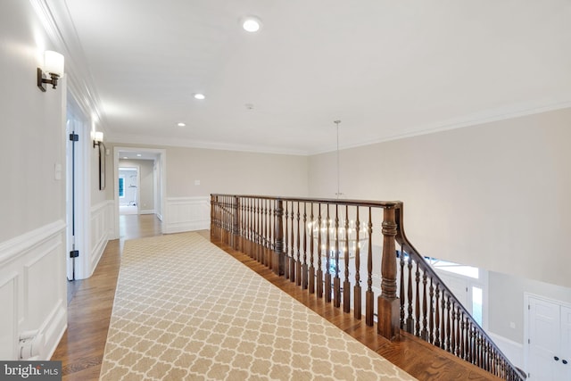 hallway featuring crown molding, wainscoting, a decorative wall, and wood finished floors