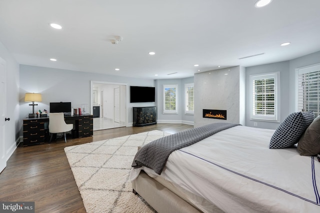 bedroom featuring a high end fireplace, wood finished floors, baseboards, and recessed lighting