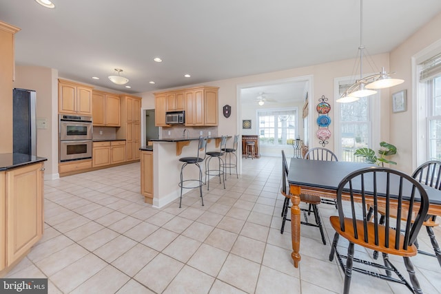 kitchen featuring dark countertops, appliances with stainless steel finishes, a kitchen breakfast bar, and light brown cabinetry